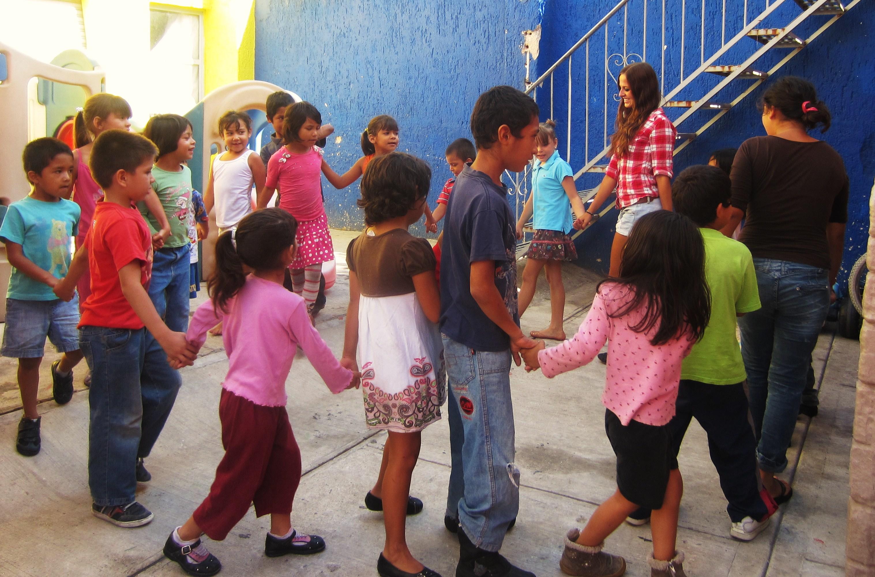 Projects Abroad Childcare volunteers hold hands with children in Mexico during an educational activity at a care centre. A group of Projects Abroad volunteers working with children in Mexico hold children's hands during an activity at a care centre.